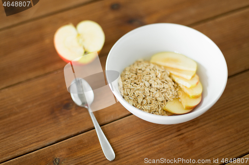 Image of oatmeal in bowl with apple and spoon on table
