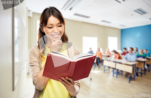 Image of happy asian woman reading book at school
