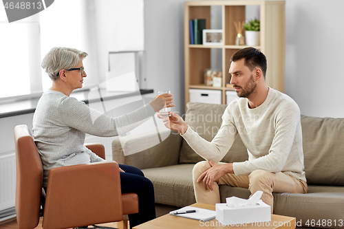 Image of senior psychologist giving water to man patient