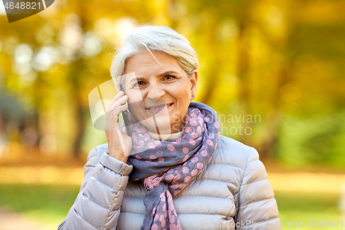 Image of senior woman calling on smartphone at autumn park