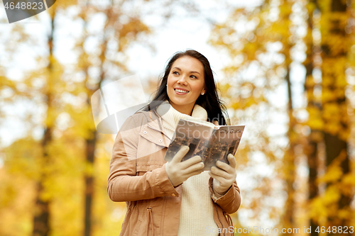 Image of happy young woman with city guide in autumn park