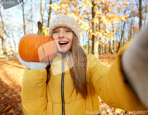 Image of girl with pumpkin taking selfie at autumn park