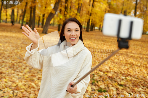 Image of woman taking selfie by smartphone at autumn park