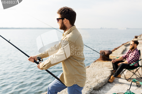 Image of male friends with fishing rods on sea pier