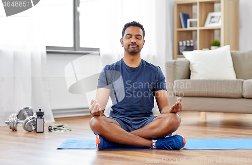 Image of indian man meditating in lotus pose at home