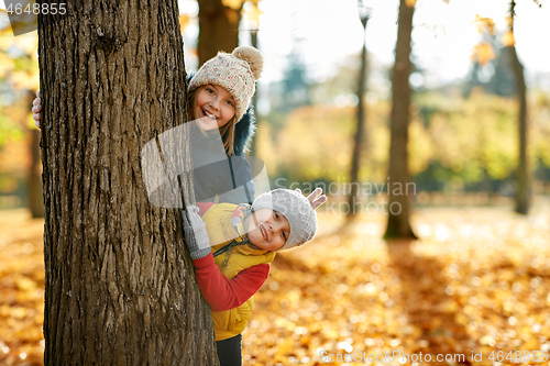 Image of happy children peeking out tree at autumn park