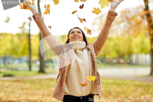 Image of happy woman having fun with leaves in autumn park