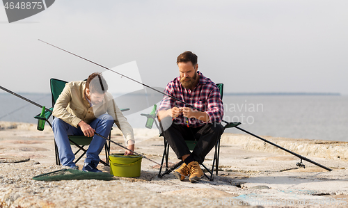 Image of friends adjusting fishing rods with bait on pier