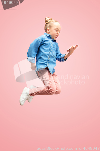 Image of Young happy caucasian teen girl jumping with phone in the air, isolated on pink studio background.