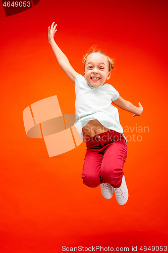 Image of Young happy caucasian teen girl jumping in the air, isolated on red studio background.