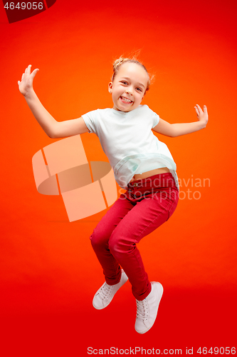 Image of Young happy caucasian teen girl jumping in the air, isolated on red studio background.