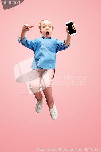 Image of Young happy caucasian teen girl jumping with phone in the air, isolated on pink studio background.