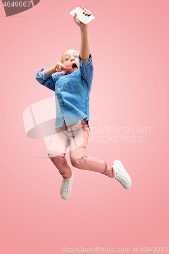 Image of Young happy caucasian teen girl jumping with phone in the air, isolated on pink studio background.