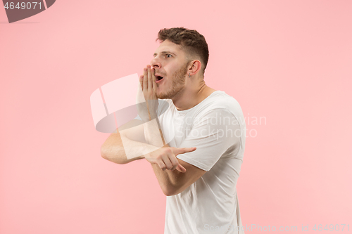 Image of The young man whispering a secret behind her hand over pink background