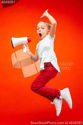 Image of Beautiful young child teen girl jumping with megaphone isolated over red background