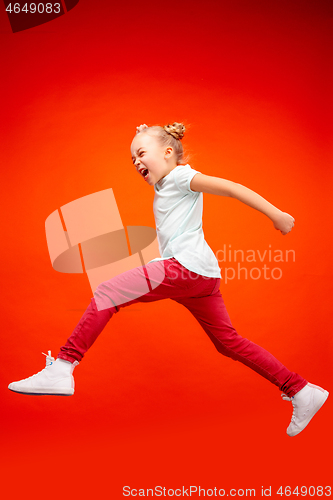 Image of Young happy caucasian teen girl jumping in the air, isolated on red studio background.