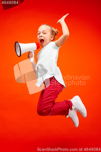 Image of Beautiful young child teen girl jumping with megaphone isolated over red background