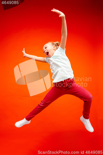 Image of Young happy caucasian teen girl jumping in the air, isolated on red studio background.