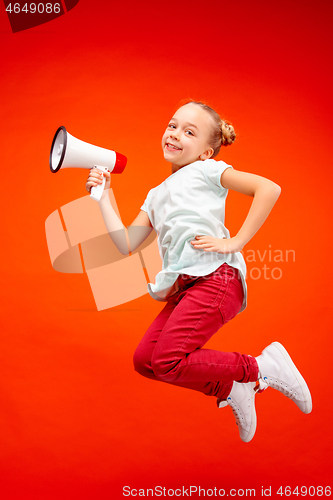 Image of Beautiful young child teen girl jumping with megaphone isolated over red background
