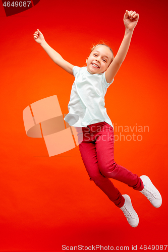 Image of Young happy caucasian teen girl jumping in the air, isolated on red studio background.
