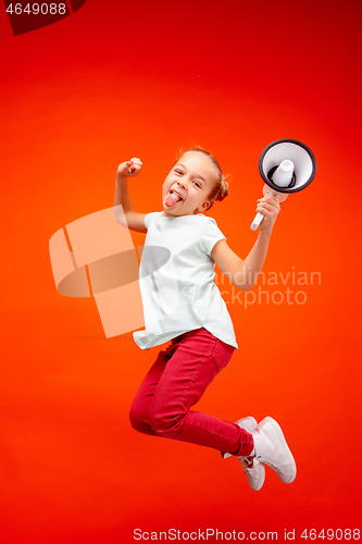 Image of Beautiful young child teen girl jumping with megaphone isolated over red background