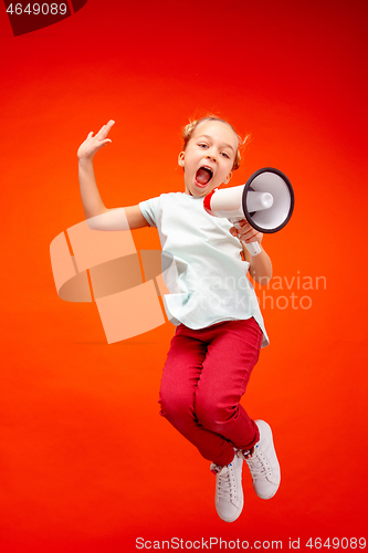 Image of Beautiful young child teen girl jumping with megaphone isolated over red background