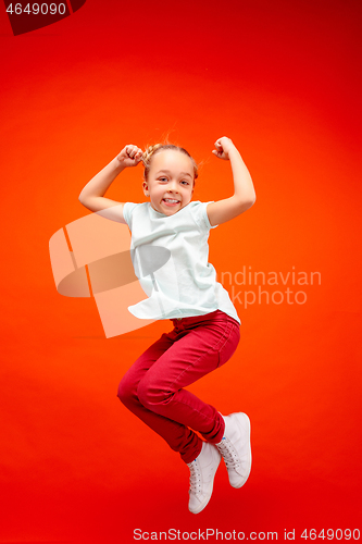 Image of Young happy caucasian teen girl jumping in the air, isolated on red studio background.