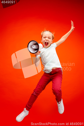 Image of Beautiful young child teen girl jumping with megaphone isolated over red background