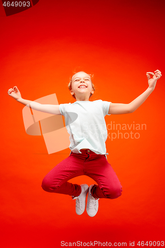 Image of Young happy caucasian teen girl jumping in the air, isolated on red studio background.
