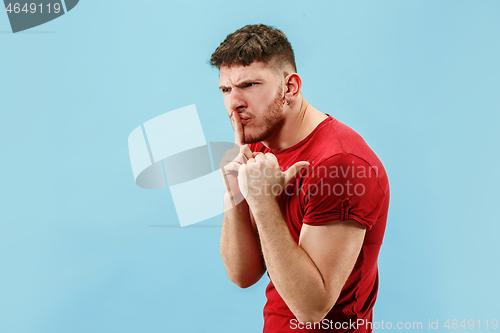 Image of The young man whispering a secret behind her hand over blue background