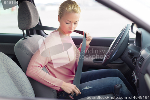 Image of Beautiful woman fastening seat belt in small personal car.