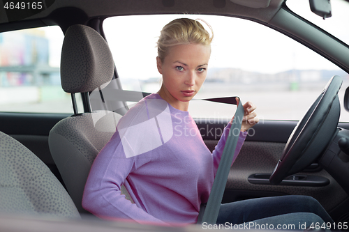 Image of Beautiful woman fastening seat belt in small personal car.