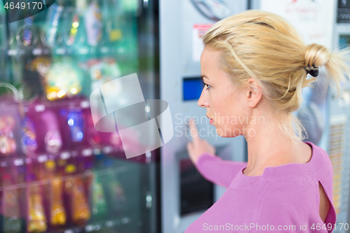 Image of Caucasian woman using a modern vending machine. Her right hand is placed on the dia pad