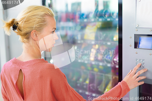 Image of Caucasian woman using a modern vending machine. Her right hand is placed on the dia pad