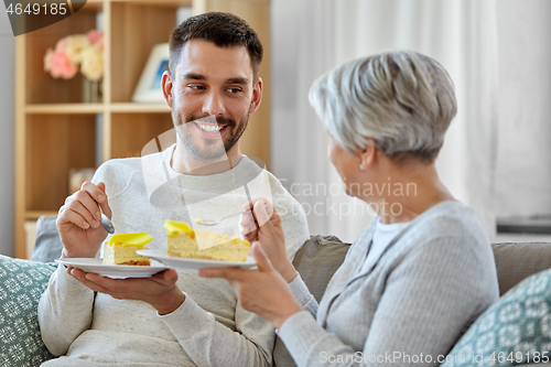 Image of senior mother and adult sun eating cake at home