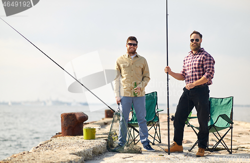 Image of happy friends with fishing rods and beer on pier