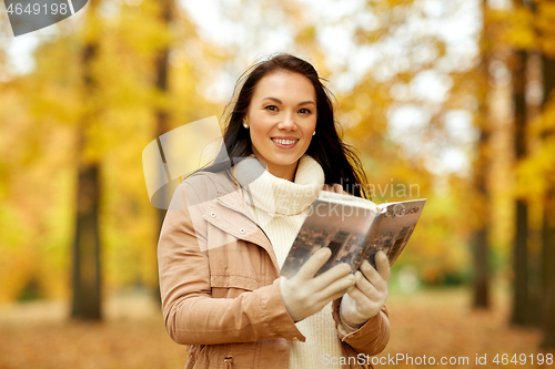 Image of happy young woman with city guide in autumn park