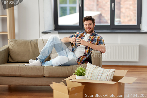 Image of man with boxes and drinking coffee at new home