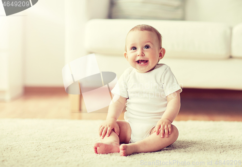 Image of happy baby boy or girl sitting on floor at home