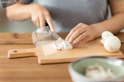 Image of woman cutting champignons by knife on board