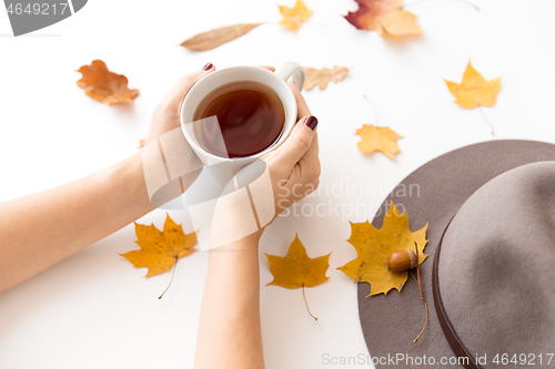 Image of hands with cup of tea, autumn leaves and hat