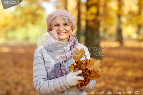 Image of senior woman with maple leaves at autumn park