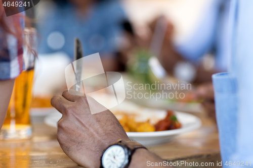 Image of african man eating with friends at restaurant