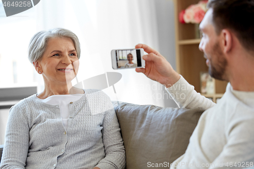 Image of adult son photographing senior mother at home