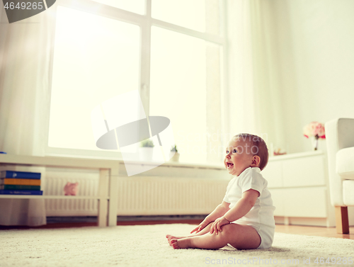 Image of happy baby boy or girl sitting on floor at home