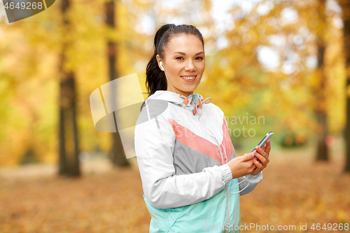 Image of woman in autumn park and listening to music