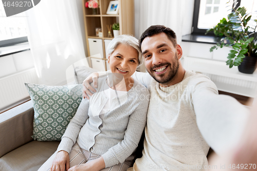 Image of senior mother with adult son taking selfie at home