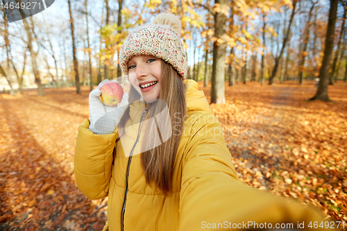 Image of happy girl with apple taking selfie at autumn park