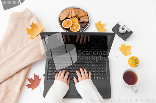 Image of woman\'s hands typing laptop, tea and autumn leaves