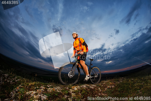 Image of cyclist standing with mountain bike on trail at sunset